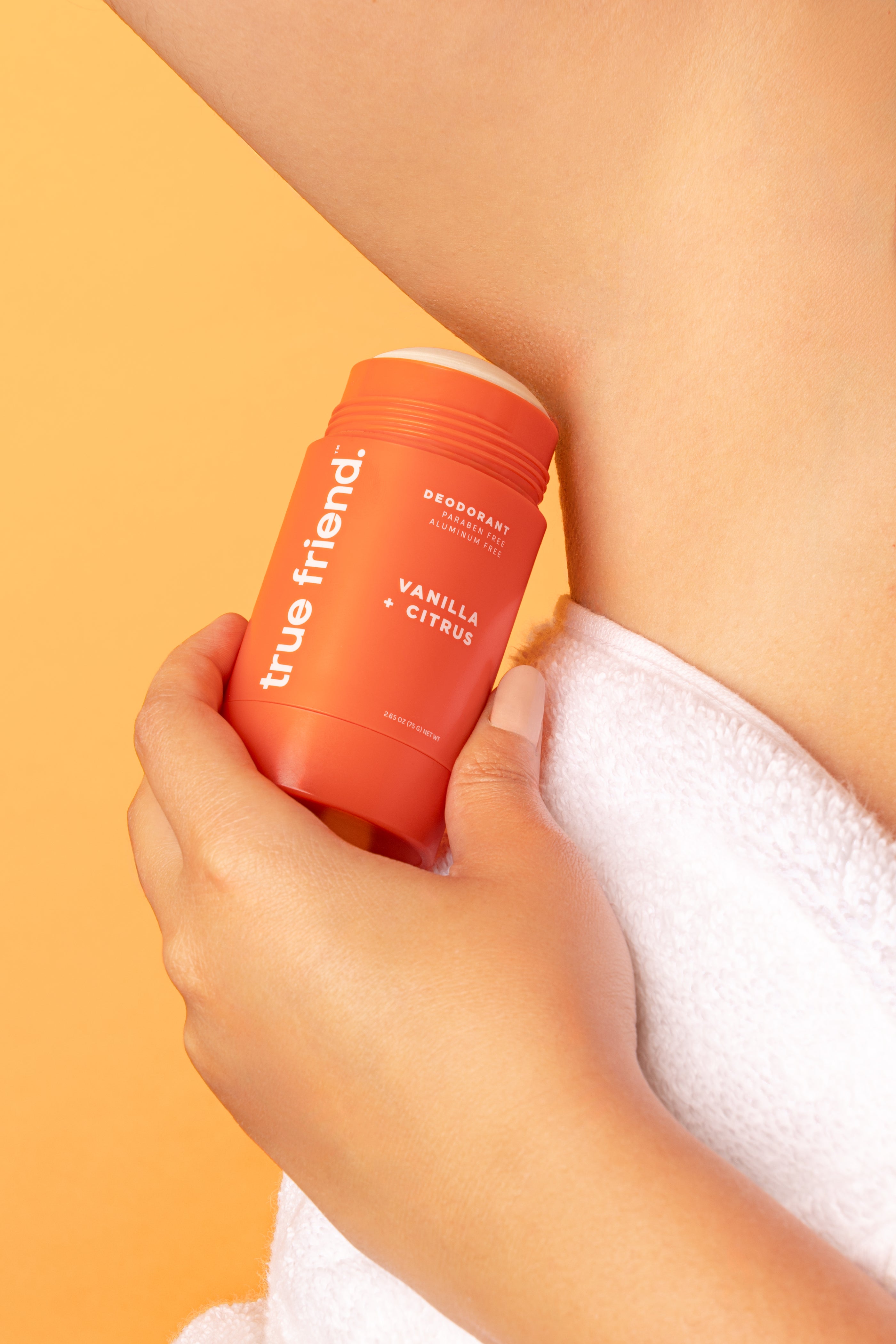 woman holding True Friend vanilla + citrus deodorant to her armpit