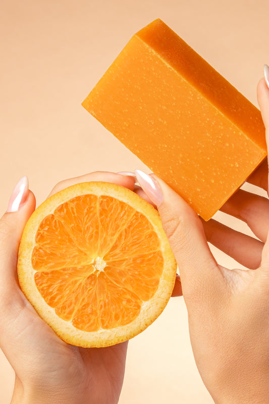 Hands holding an orange in the left hand and a True Friend citrus soap bar in the right hand