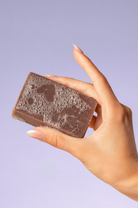 Hand holding a purple, lavender True Friend soap bar
