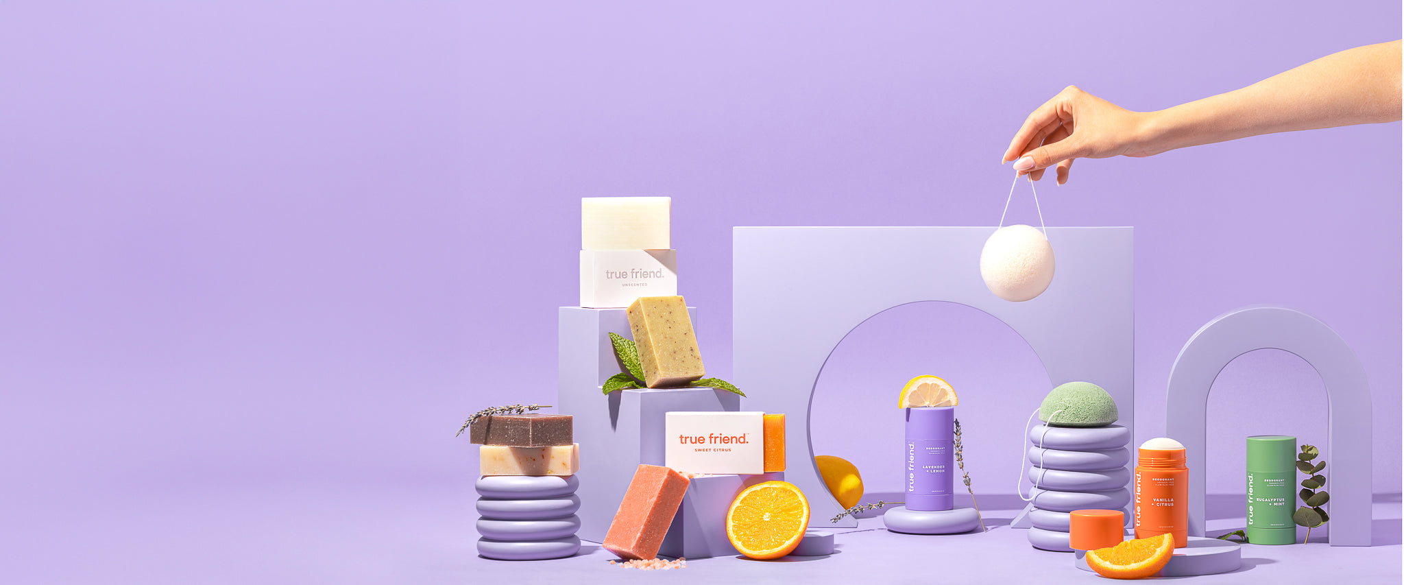 Full collection of True Friend products: organic soap bars, nontoxic True Friend deodorants, and konjac sponges on a purple background