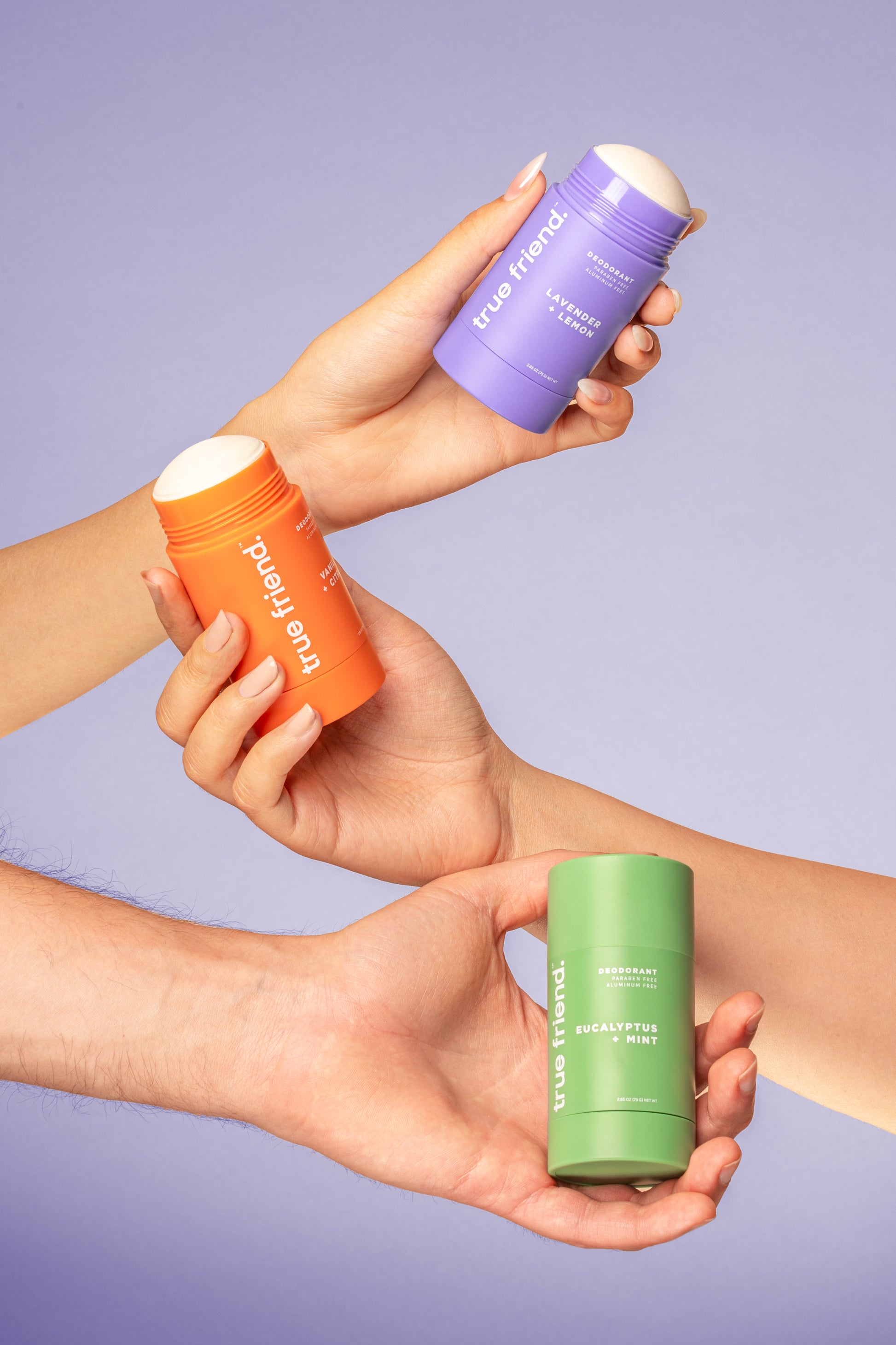 Three hands holding True Friend deodorant containers in the scents of lavender + lemon, vanilla + citrus, and eucalyptus + mint 