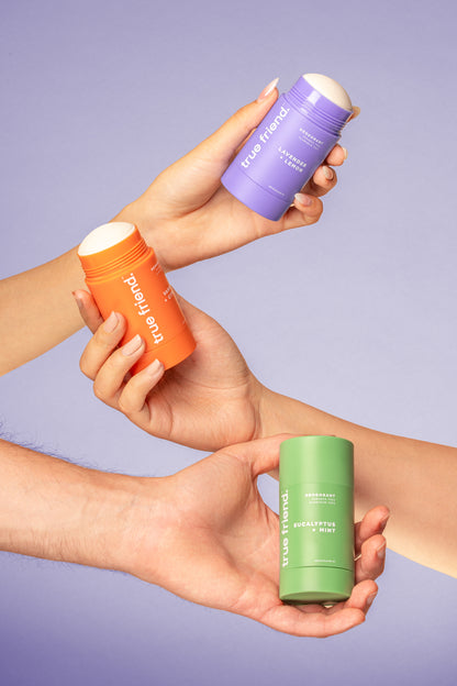 Three hands holding True Friend deodorant containers in the scents of lavender + lemon, vanilla + citrus, and eucalyptus + mint 