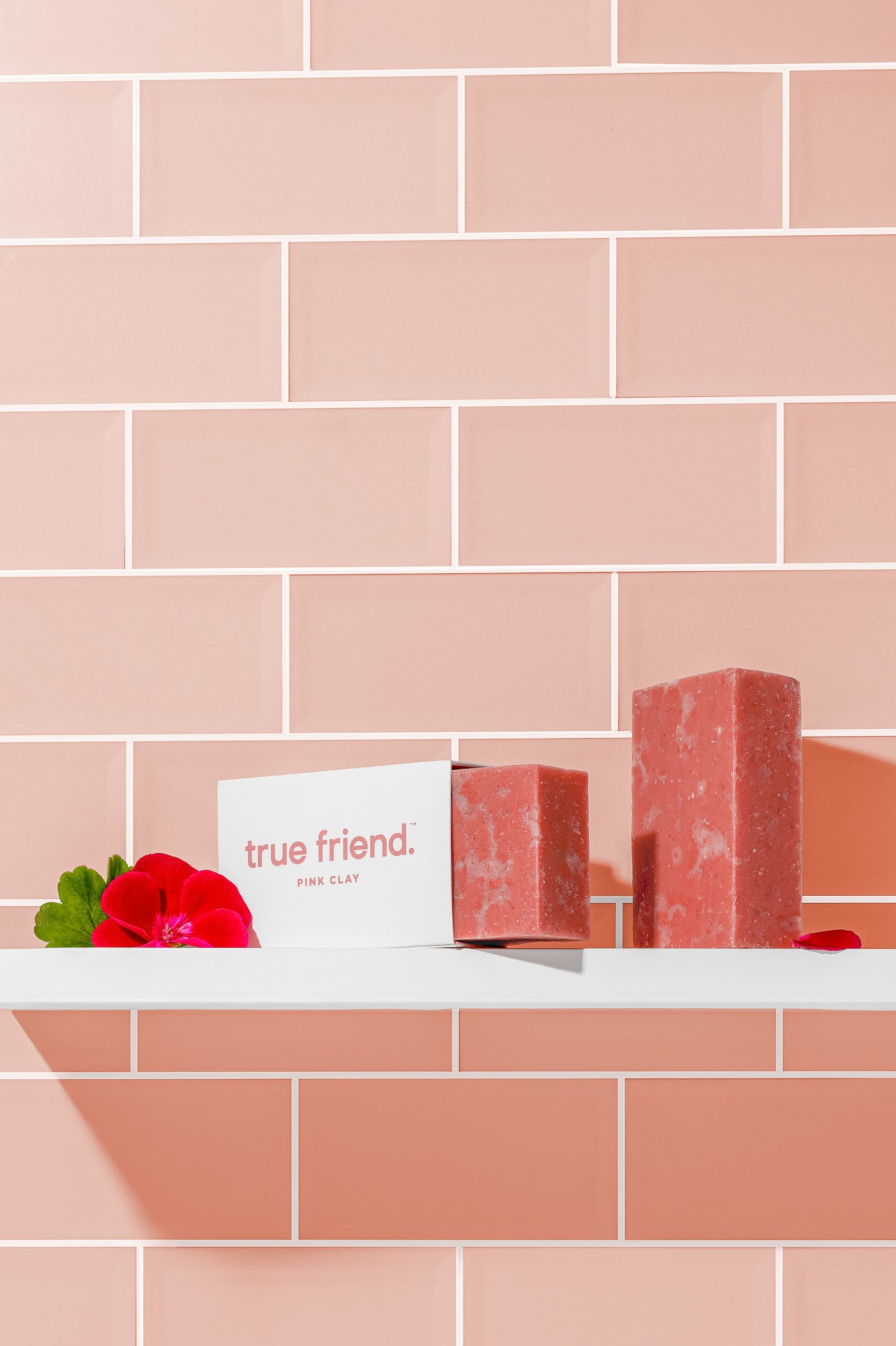 Two pink clay True Friend soap bars sitting on a bathroom shelf with pink tile background