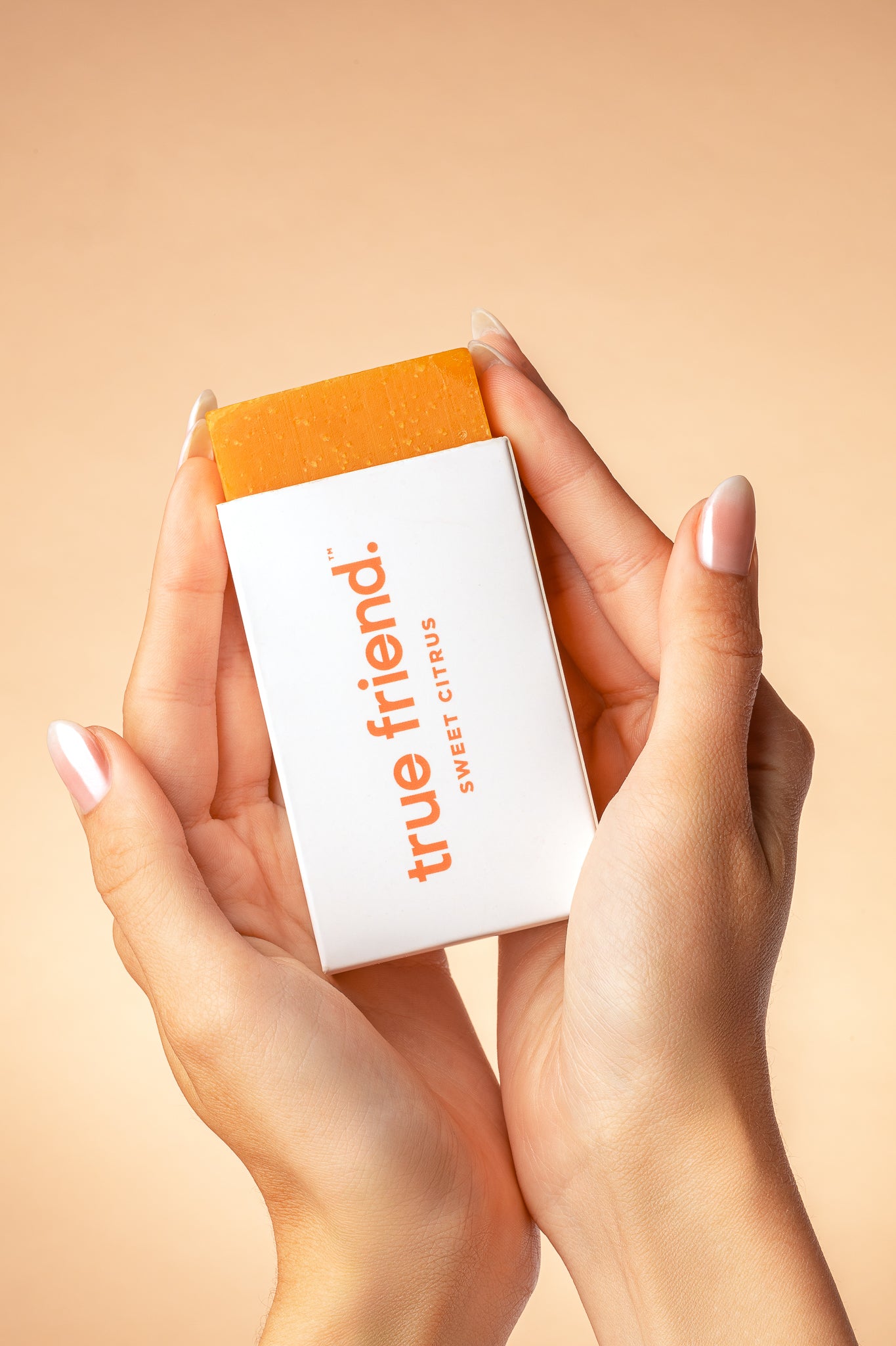 Hands holding True Friend citrus soap bar with orange background