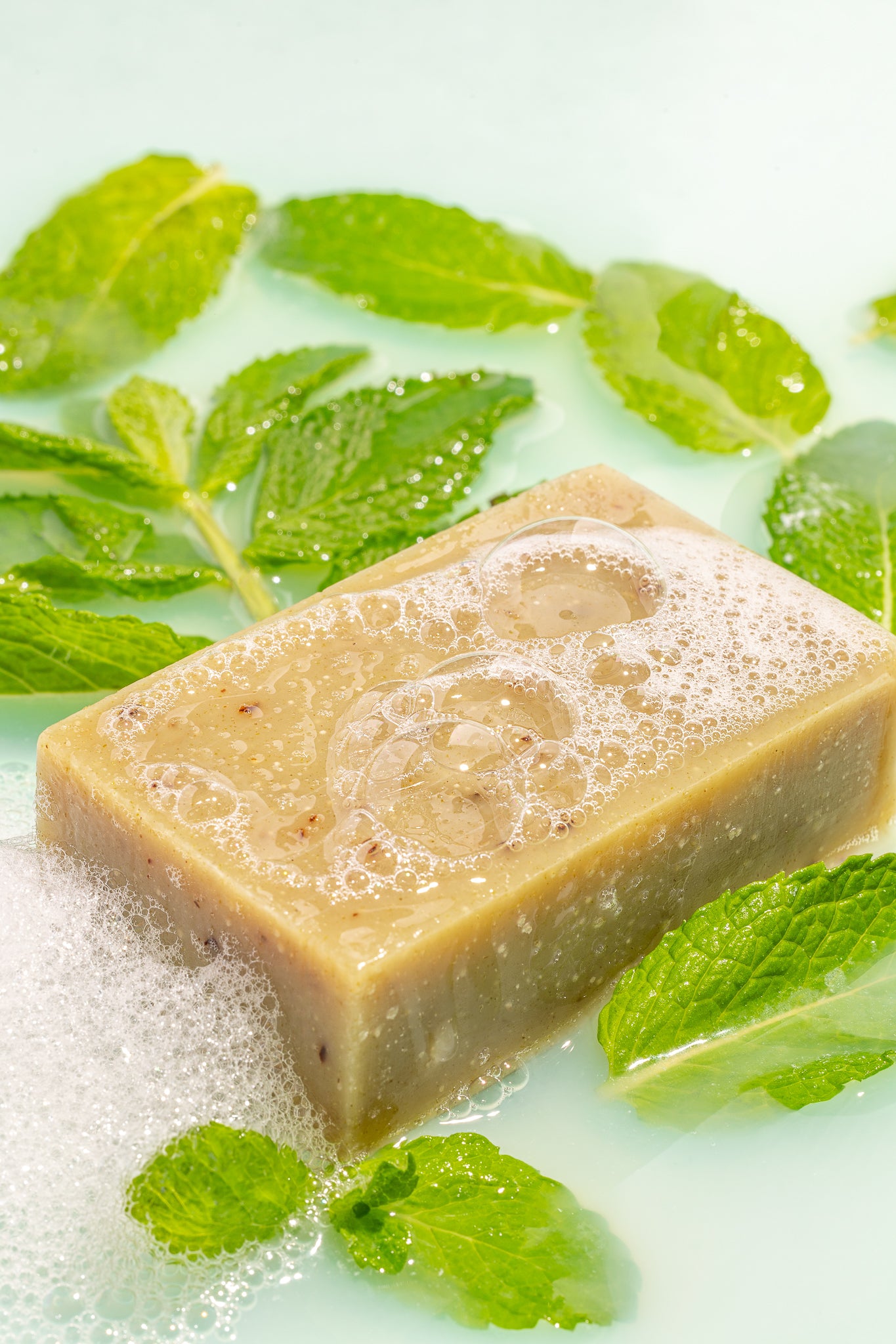 True Friend peppermint soap bar in water with peppermint leaves around the bar