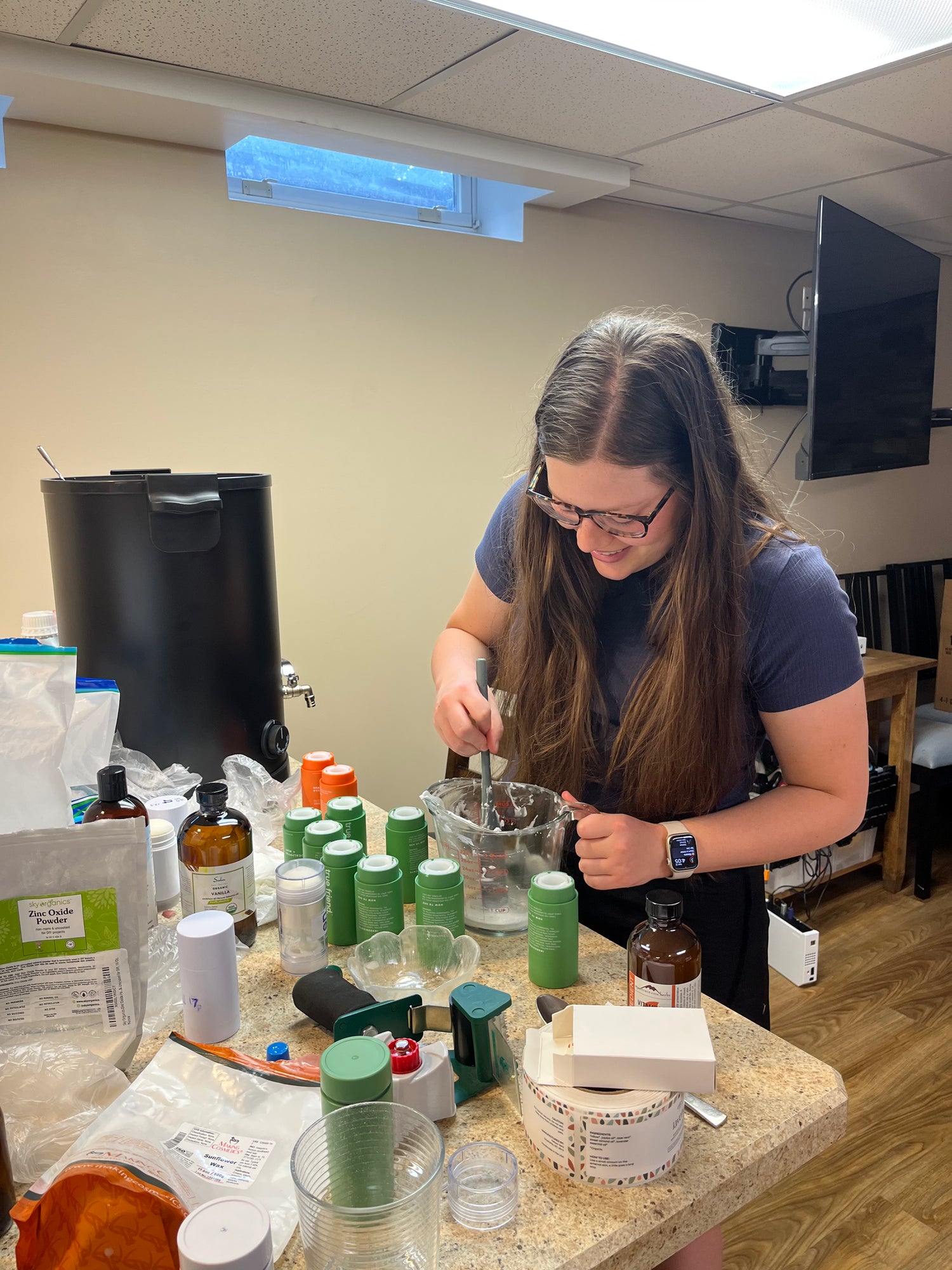 Person working at a counter with various bottles and containers in a room setting.
