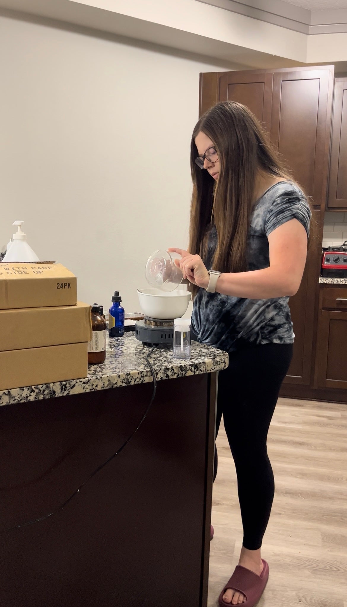 Woman pouring a substance into a container on a counter with boxes and bottles around.