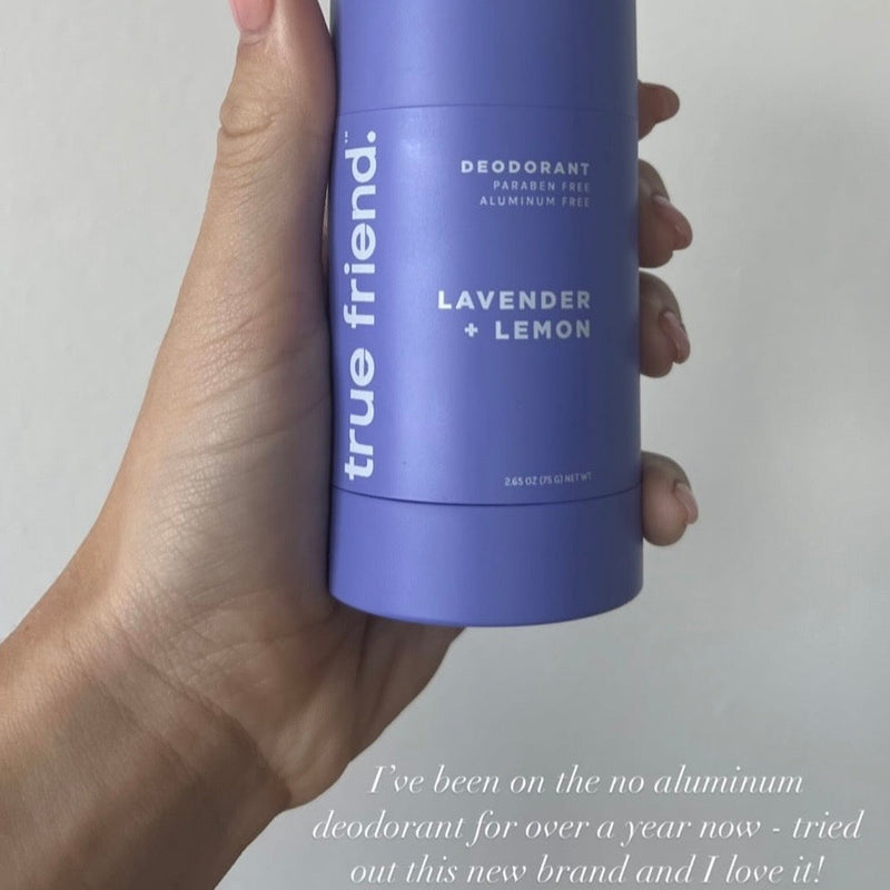 Hand holding a purple deodorant stick labeled 'true friend' with lavender and lemon scent on a light gray background.